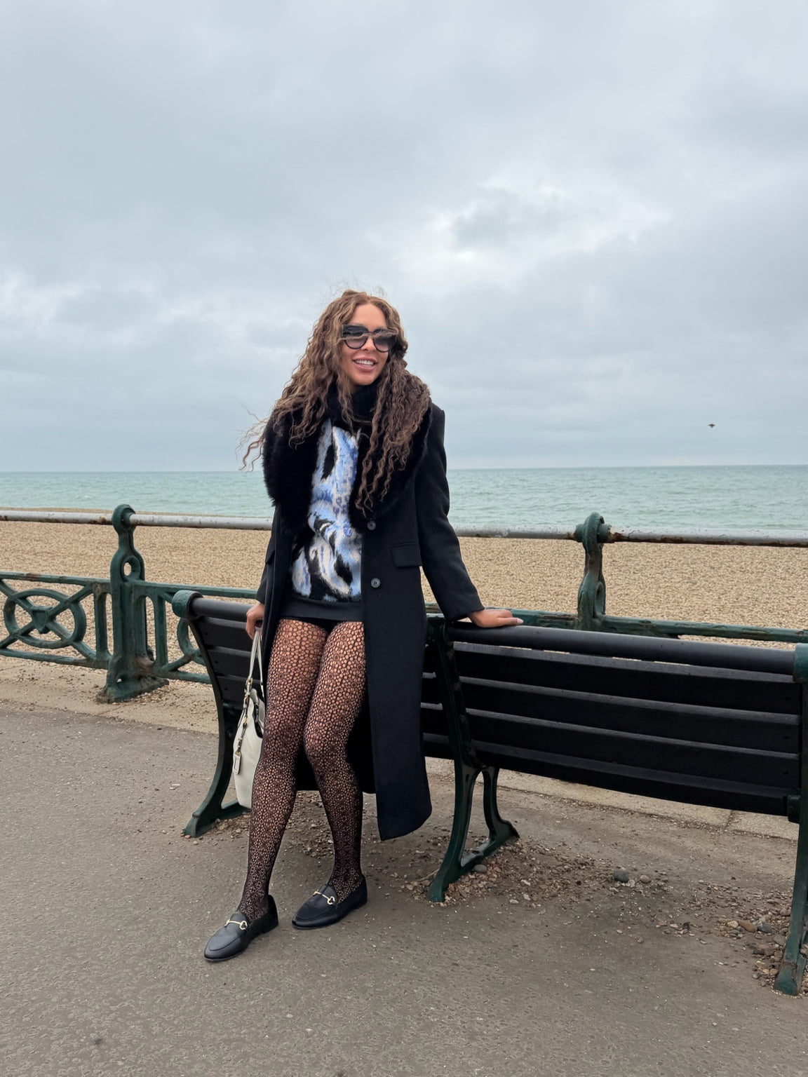 Model wearing black Lace Loop openwork tights with a black coat and loafers on Brighton seafront