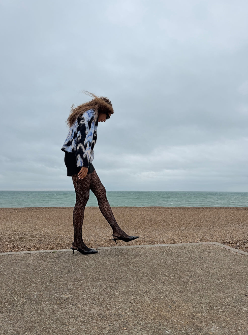 Model wearing black Lace Loop openwork tights on Brighton seafront, walking along the promenade